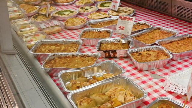 At the Eastern Market in Genoa, Italy, a stall selling local specialties of savory pies and meatballs, the tags list meatloaf, asparagus, Russian salad, and prices. The gaze runs along the counter.