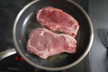 Close-up of raw ribeye steaks cooking in a pan, showcasing the texture and marbling, ideal for food-related content, culinary guides, and steak preparation techniques