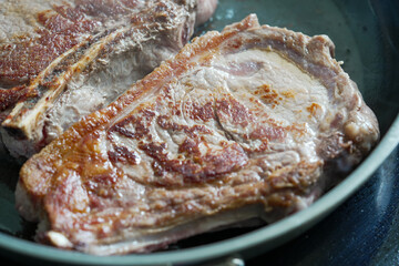 Raw ribeye steaks cooking in a hot pan, emphasizing the marbling and texture,