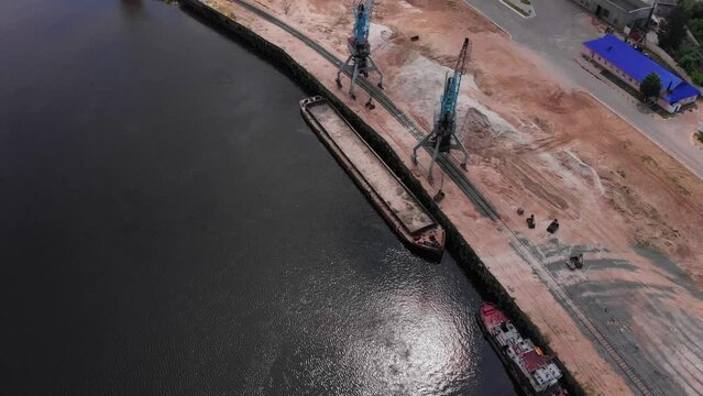 Aerial view of a river port where cranes load a barge with sand. The scene captures the activity and infrastructure of the port area.