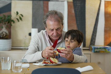Grandfather teaching young boy how to peel an apple with a red knife, sharing quality family time...