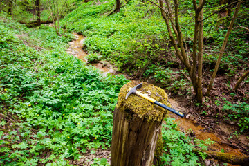 View of a small stream flowing through a ravine and a pickaxe lying on a decrepit stump,...