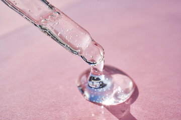 Pipette with serum shimmering in the sun on a pink background.