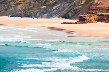 Waves on the coast of Atlantic ocean in Algarve, Portugal. Beach with yellow sand and turquoise water.