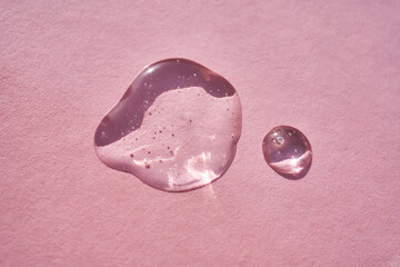 Drop of serum shimmering in the sun on a pink background.