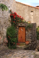 Fototapeta premium House front in village in Pyrenees mountains in southern France featuring wooden door adorned with red geraniums in blossom