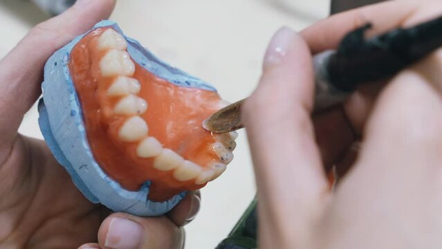 A dental technician is shown crafting dentures by soldering and shaping teeth with precision in a laboratory setting, focusing on the detailed work.