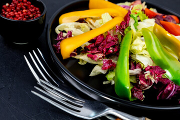 vegan salad of leaves and sweet peppers on a black plate