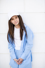 Cute teenage girl 10 - 12 year old wearing cap and blue shirt on city street over white wall...