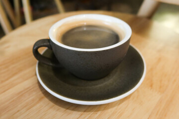 close up of black mug cup with hot black americano coffee on a wooden table.