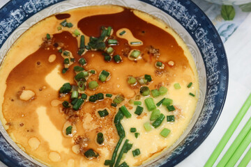 close up homemade Hong Kong Chinese style steamed egg with soy sauce, spring onion and oil in a blue and white china dish