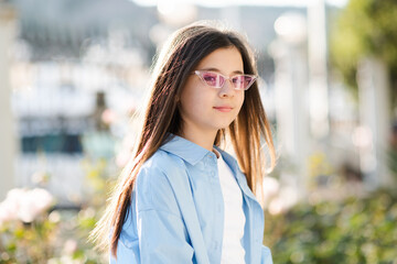 Stylish teenage girl 10 - 12 year old wearing sun glasses and blue shirt posing over nature sunny...