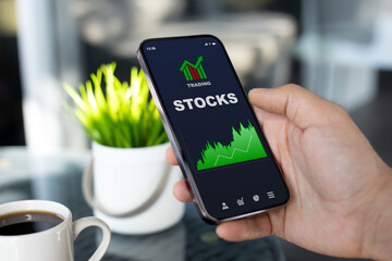 Man hand hold phone with stocks trading app on screen