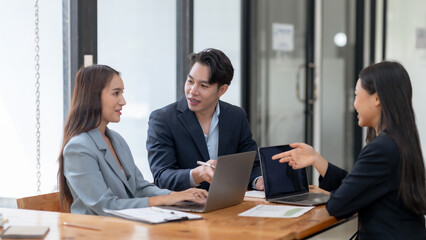 Business meeting with three professionals discussing strategy and collaboration while using laptops in a modern office setting.