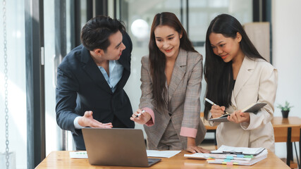 Three business colleagues are engaged in a meeting, reviewing documents and discussing strategies in a modern office setting, showing teamwork and productivity