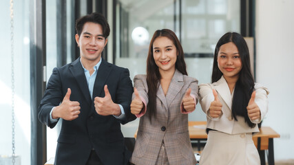 Three business colleagues are standing together and giving a thumbs up in a modern office, showing a positive and successful outcome of their teamwork