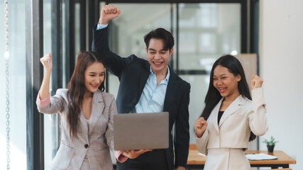 Three business colleagues are celebrating their success with joyful expressions and raised fists,...