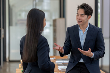 Two business professionals in formal attire discussing work-related matters in a modern office environment, displaying teamwork and collaboration.