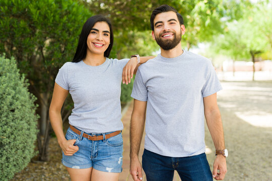 Attractive hispanic couple in plain gray t-shirts posing together in a park, ideal for mockup designs - Powered by Adobe