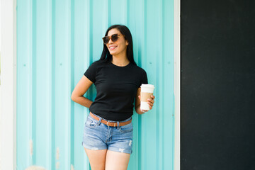 Confident latin woman in black t-shirt holding coffee cup stands against teal background with...
