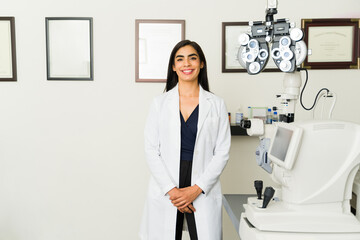 Skilled Latin ophthalmologist ready to see patients in her clinic, smiling with advanced eye...