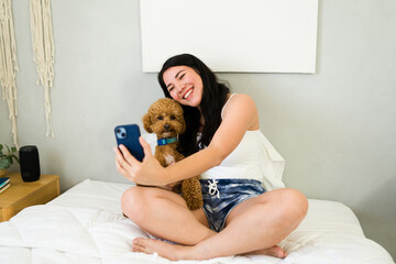 Happy woman snaps a selfie with her cute brown poodle in a comfortable, warmly lit bedroom scene
