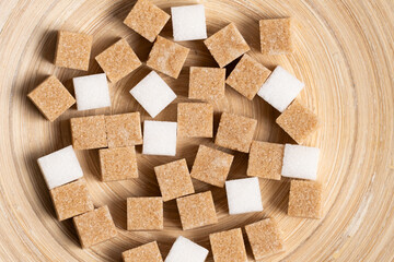 Cubes of cane and white refined sugar on wooden background.