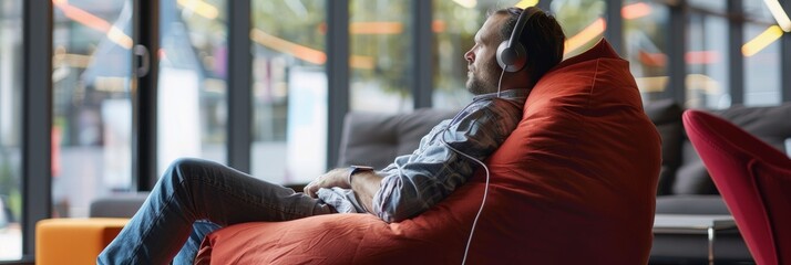 A man wearing headphones sits on a bean bag chair, deeply engrossed in listening to music