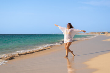 Beautiful woman with arms raised and outstretched walking on sunny beach
