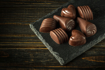 Sweet dark chocolate candies on a serving board. Space for advertising on a black rustic table