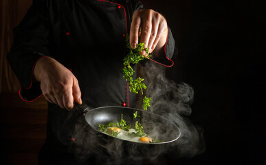 A professional chef throws fresh aromatic parsley into scrambled eggs in a hot frying pan with his...