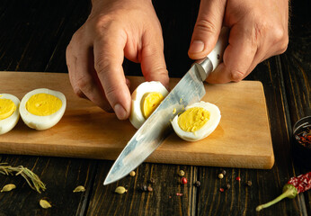 Egg diet concept. Slicing eggs with a knife in the hands of a chef on a kitchen board.