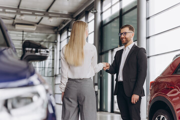 Happy woman buying a car and closing the deal with a handshake with the salesman at the dealership