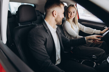 Competent car dealer showing female customer interior of luxury auto. Caucasian man and woman...