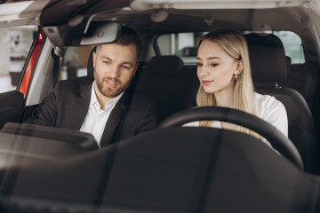 Competent car dealer showing female customer interior of luxury auto. Caucasian man and woman sitting inside and talking. Concept of selling and purchase.