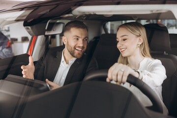Competent car dealer showing female customer interior of luxury auto. Caucasian man and woman...