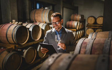 Adult man winemaker hold glass stand between the barrels in cellar