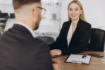 Smiling happy female manager car salesman in car dealership signing contract at table with male buyer in suit