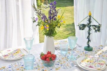 A bouquet of wildflowers and strawberries on the table for the Midsommar holiday.