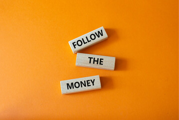 Follow the Money symbol. Concept word Follow the Money on wooden cubes. Beautiful orange...