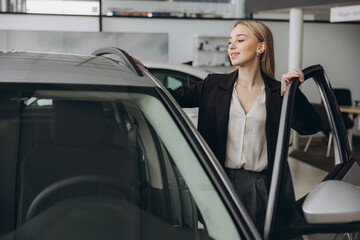 Happy amazed woman customer female buyer client wears suit open door chooses auto wants to buy new automobile in car showroom vehicle salon dealership store motor show indoor