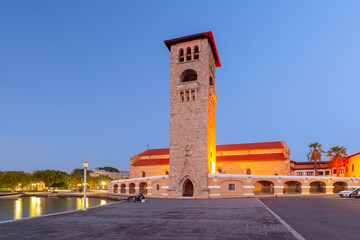 Evangelismos Church in Rhodes, Greece at twilight. Illuminated bell tower and serene waterfront view