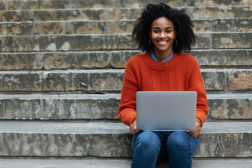 A woman smiling while working on her laptop outdoors