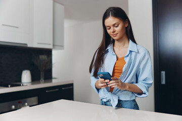 A woman checking her cell phone while standing in front of a kitchen counter in a modern home