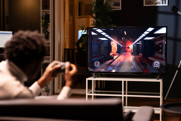 Gamer using controller to play first person shooter videogame on smart TV, shooting robotic...
