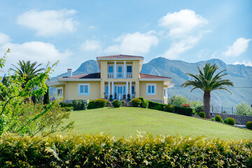 The backyard of a classic spanish cottage in front of a green lawn, trees, palms. House on the hill under the mountains in Asturia.