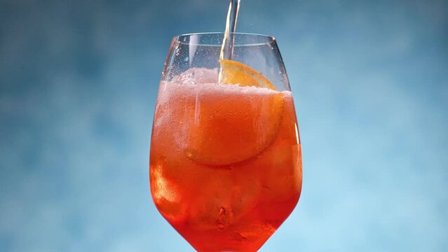 Glass of apperol spritz cocktail with orange slice on blue background. Closeup of summer drink, zoom in
