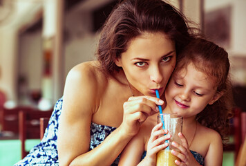Cute kid girl with happy beautiful mother drinking tasty healthy juice together with love in street...