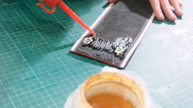 The master applies glue to the black surface of the leather blank on a green mat