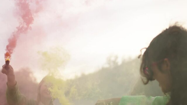 Young cheerful Caucasian lesbian woman enjoying and celebrating gay pride day with LGBT people outdoor. Diverse friends jumping and dancing together colorful smoke flare. Gen z inclusive community
